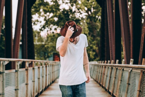 mens-fashion-walking-across-bridge-holding-hat Καπέλο Ανδρικό