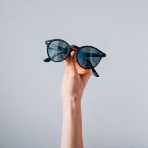 pair-of-sunglasses-held-in-front-of-grey-background Γυαλιά Ηλίου Γκρι