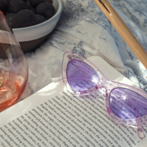 purple-retro-sunglasses-lay-on-a-open-novel-in-the-sunshine Γυαλιά Ηλίου Μωβ