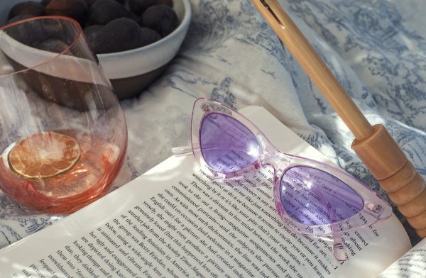 purple-retro-sunglasses-lay-on-a-open-novel-in-the-sunshine Γυαλιά Ηλίου Μωβ