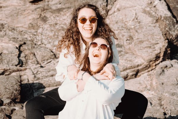 two-people-in-sunglasses-sit-in-front-of-a-large-brown-rock Γυαλιά Ηλίου Καφέ