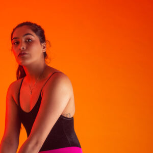 woman-wearing-black-vest-poses-against-orange-background Γιλέκο Μαύρο